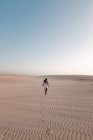 Vue arrière d'une touriste anonyme en robe blanche se promenant sur du sable côtelé sous un ciel clair — Photo de stock