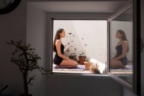 Full length barefoot female sitting on Thunderbolt Pose on yoga mat with eyes closed on sunny balcony and meditating — Stock Photo