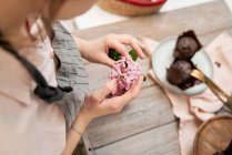 High angle of crop anonymous female with blossoming flower sprig above table with baked dessert during cooking process at home — Stock Photo