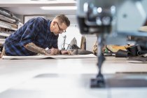 Передвижная стопа и иглопластина потёртой швейной машинки на рабочем столе на фоне человека, работающего в мастерской по обивке — стоковое фото