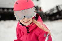 Positivo ragazza carina in rosa caldo activewear occhiali e casco sci accanto pista innevata sulla chiara giornata invernale — Foto stock