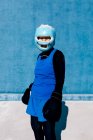 Reife Frau in Sportbekleidung und Boxhandschuhen steht mit Helm vor blauer Wand und blickt in die Kamera — Stockfoto
