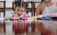 Crop unrecognizable woman and little child sitting at table and drawing with markers in notebook — Stock Photo
