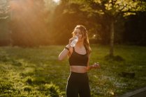 Young sportswoman drinking water during break from training in back lit — Stock Photo