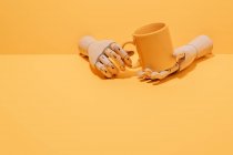 Творча декоративна дерев'яна рука тримає барвистий кухоль на жовтому фоні в студії — стокове фото