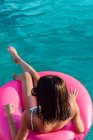 Giovane allegra viaggiatrice in costume da bagno e occhiali da sole sdraiata in anello gonfiabile in piscina — Foto stock