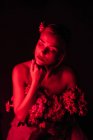 Приваблива молода гола пліч-о-пліч жінка в білих штанях з букетом свіжих барвистих квітів, що сидять на табуреті проти яскравого неонового світла в темній студії з закритими очима — стокове фото