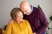 Fröhliches Paar mittleren Alters, das sich zu Hause umarmt, während es Zeit miteinander verbringt und das Wochenende genießt — Stockfoto