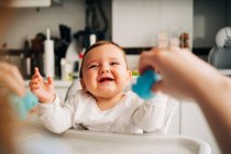 Niedliches lachendes Baby in weißem Hemd sitzt im Babystuhl in der modernen Küche — Stockfoto