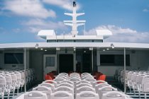 Terrazzo di barca da crociera con sedie bianche vuote in fila sotto cielo limpido con nuvole — Foto stock
