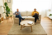 Alto angolo di uomo maturo utilizzando smartphone e tablet di navigazione donna di mezza età mentre seduto sul divano in soggiorno a casa — Foto stock