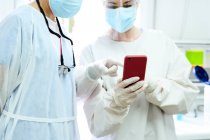 Chirurghi femminili in tappi di stoffa medica navigazione internet sul cellulare contro computer desktop in ospedale luce — Foto stock