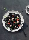 Von oben schwarze Tuschspaghetti mit Lachs in Keramikteller auf dunklem Hintergrund — Stockfoto