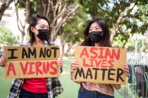 Етнічні жінки в масках тримають плакати, що протестують проти расизму на міській вулиці і дивляться геть — стокове фото
