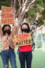Des femmes ethniques portant des masques portant des affiches protestant contre le racisme dans la rue de la ville et regardant la caméra — Photo de stock
