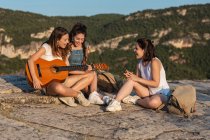Grupo de caminhantes femininas sentadas na colina em terras altas enquanto tocavam guitarra acústica e cantavam canções — Fotografia de Stock