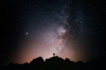 Силует анонімного туриста, що стоїть на скелі на тлі сяючого зоряного неба вночі — стокове фото