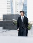 Jovem executivo étnico masculino de casaco com a mão no bolso e netbook olhando para longe enquanto passeia na cidade — Fotografia de Stock