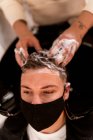 Зверху врожаю анонімний перукар з татуюваннями миття волосся людини з шампунем в умивальнику в перукарні — стокове фото