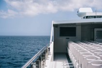 Deck do barco de cruzeiro com cadeiras brancas vazias na fileira sob o céu desobstruído com nuvens — Fotografia de Stock