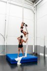 Sporty male instructor helping flexible strong sportswoman performing exercise on aerial silks in light fitness center — Stock Photo