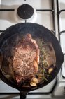 Von oben Pfanne mit appetitanregendem Fleischstück mit Gewürzen und Rosmarinzweig in geschmolzener Butter auf Gasherd — Stockfoto