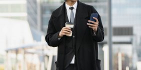 Cropped unrecognizable young well dressed ethnic male executive with cellphone and hot drink to go in city — Stock Photo