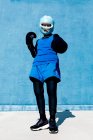 Da sotto tutta la lunghezza donna matura in abbigliamento sportivo e guanti da boxe in piedi con casco contro parete blu e guardando la fotocamera — Foto stock