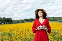 Sonriente hembra en sombrero tomando fotos en cámara vintage en el prado bajo el cielo nublado - foto de stock
