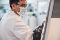 Концентрований чоловічий науковець у лабораторному пальто та масках, який тримає руки в кабінеті біобезпеки під час роботи з забрудненими матеріалами — стокове фото