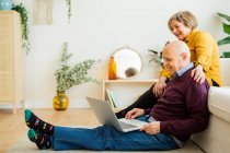Весела зріла пара розмовляє на відео чаті на ноутбуці у вітальні — стокове фото