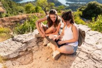 Зверху захоплені подорожуючі друзі-жінки сидять на скелі в високогір'ї і дивляться фільм на нетбуці під час літніх походів — стокове фото