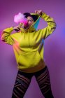 Von unten selbstbewusste Hipsterin im Kapuzenpulli, die E-Zigarette im Studio auf rosa Hintergrund raucht — Stockfoto