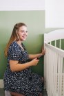 Side view woman with screwdriver leaning forward while mounting crib at home on sunny day — Stock Photo