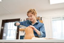 Jovem fêmea com faca afiada cortando abóbora crua na tábua de corte enquanto cozinha na cozinha em casa — Fotografia de Stock