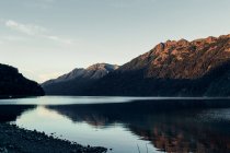 Paesaggio spettacolare di catena montuosa con foresta verde situata vicino al lago calmo con acqua increspata — Foto stock