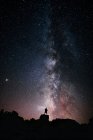 Низький кут силуету анонімного туриста, що стоїть зі світловим факелом на голові на скелі проти сяючого зоряного неба вночі — стокове фото