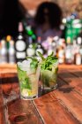 Glasses of refreshing mojito cocktails with ice and mint served on outdoor wooden bar counter — Stock Photo