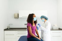 Ärztin in Schutzuniform, Latexhandschuhen und Gesichtsmaske impft afroamerikanische Patientin in Klinik während des Coronavirus-Ausbruchs — Stockfoto