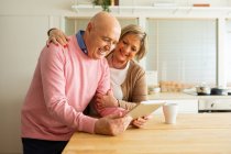 Donna di mezza età che parla con l'uomo utilizzando tablet mentre in piedi insieme in cucina a casa — Foto stock