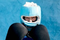 Donna matura in abbigliamento sportivo e guanti da boxe in piedi con casco contro il muro blu e guardando la fotocamera — Foto stock
