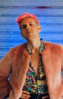 Giovane uomo omosessuale in abito alla moda con manicure e taglio di capelli moderno guardando la fotocamera su sfondo blu — Foto stock