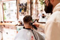 Мужчина-парикмахер в очках делает стрижку для взрослого клиента в парикмахерской во время пандемии COVID 19 — стоковое фото