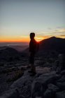 Escursionista maschio senza volto a tutta lunghezza con zaino ammirando panoramico terreno montagnoso e in piedi sulla vetta rocciosa ruvida al tramonto a Siviglia Spagna — Foto stock