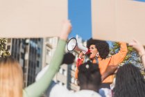 Afrikanisch-amerikanische Kämpferin für soziale Gerechtigkeit mit einem Sprecher gegen die Ernte anonyme multirassische Menschen mit Plakaten kämpfen für die Menschenrechte in der Stadt — Stockfoto