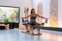 Konzentriert durchtrainierte weibliche Dehnbeine und Ausfallübungen auf dem Pilates-Reformer beim Training im Fitnessstudio — Stockfoto