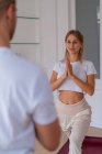 Content couple in activewear standing on mats in Anjaneyasana with Namaste gesture while doing yoga in morning and looking at each other — Photo de stock