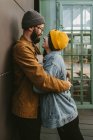 Вид сбоку на молодую стильную пару, мягко обнимающуюся, стоя на деревянной террасе возле дома — стоковое фото