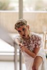 Young female in stylish bohemian white bridal dress and high heeled boots with ornamental wreath and earrings standing on stairway and looking at camera — Photo de stock