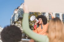 African American female social justice warrior with speaker against crop anonymous multiracial people with placards fighting for human rights in town - foto de stock